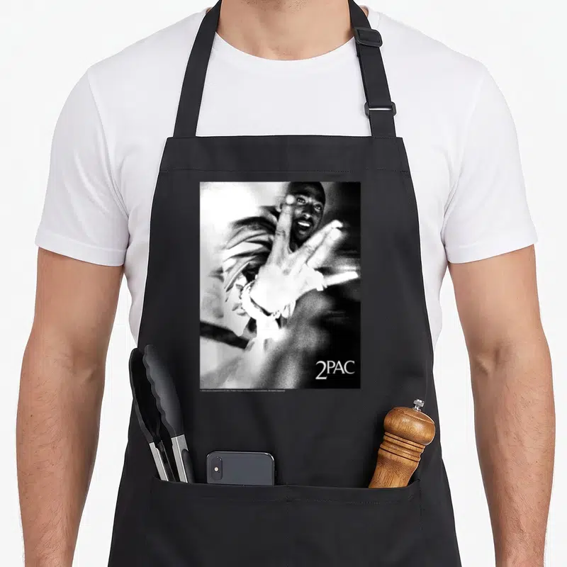 Tablier de cuisine noir avec une illustration monochrome de 2Pac tendant la main et le texte 2PAC en bas à droite.