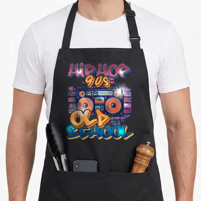 Tablier de cuisine noir avec une illustration de boombox orange et bleue sur fond de mur de briques graffité.