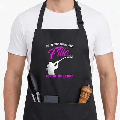 Tablier de cuisine noir avec une silhouette blanche tirant au fusil et du texte rose vif.