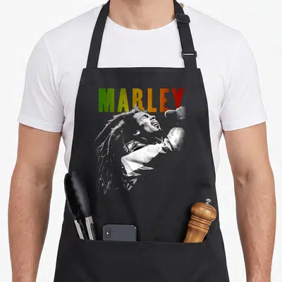 Tablier de cuisine noir avec illustration monochrome d'un chanteur aux dreadlocks et le nom MARLEY en vert jaune et rouge.