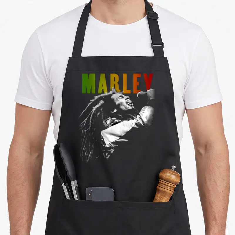 Tablier de cuisine noir avec illustration monochrome d'un chanteur aux dreadlocks et le nom MARLEY en vert jaune et rouge.