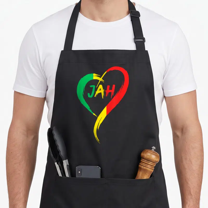 Tablier de cuisine noir avec un grand cœur aux couleurs vert jaune et rouge portant le mot Jah au centre.