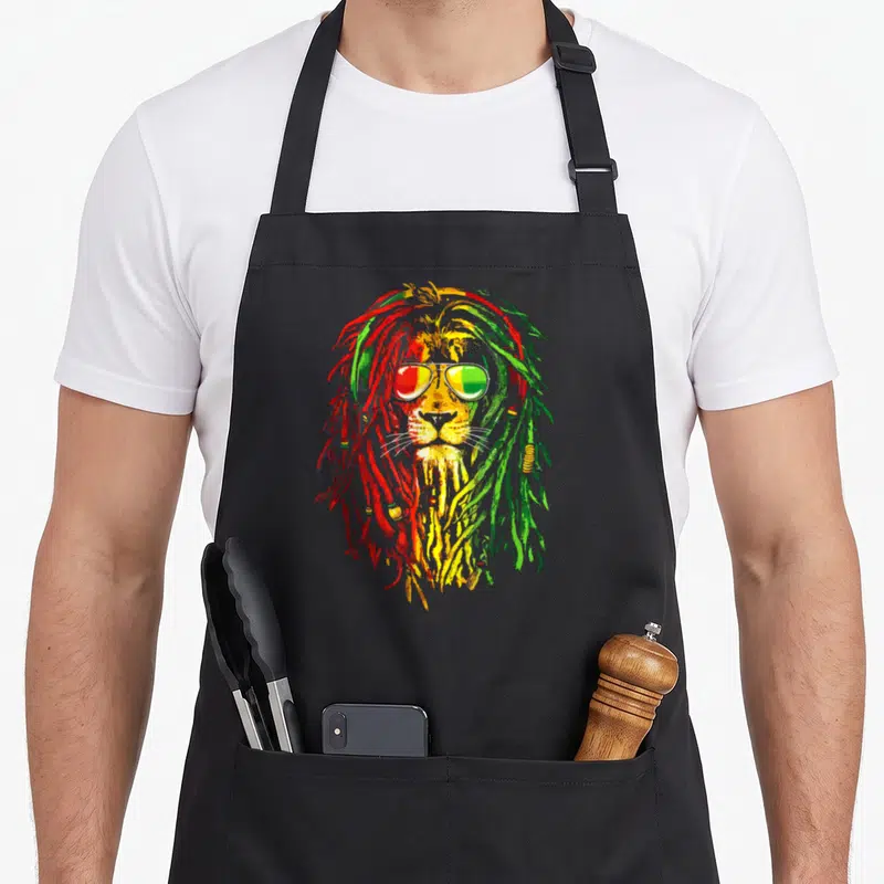 Tablier de cuisine noir avec un lion royal aux dreadlocks multicolores et lunettes de soleil aux reflets rouge vert et jaune.