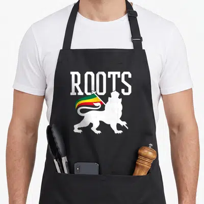 Tablier de cuisine noir avec l'inscription ROOTS et un lion blanc portant une banderole tricolore vert jaune rouge.