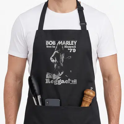 Tablier de cuisine noir avec illustration grise de Bob Marley live in Hawaii 79 et texte Reggae'sil au bas du motif.