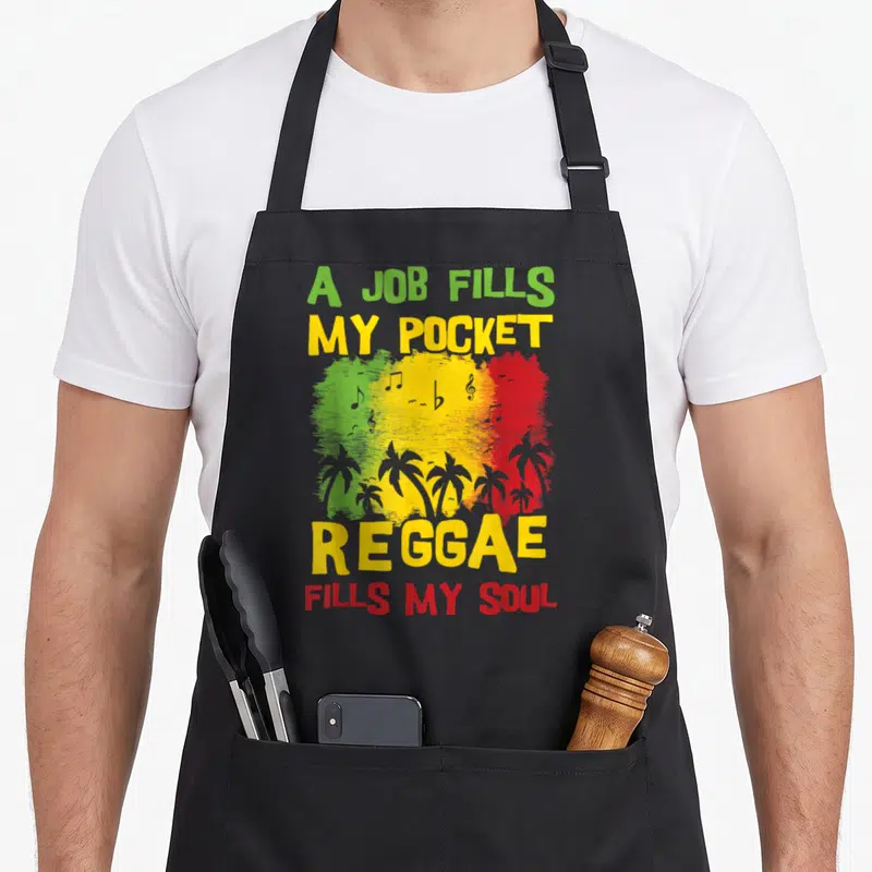 Tablier de cuisine noir avec inscription A job fills my pocket Reggae fills my soul sur fond tricolore et palmiers.