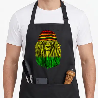 Tablier de cuisine noir avec un lion Rastafari aux dreadlocks vertes et jaunes portant un Tam rayé et des lunettes rondes.