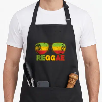 Tablier de cuisine noir avec lunettes de soleil aux couleurs rastafari et le mot REGGAE imprimé en dessous.