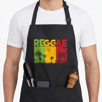 Tablier de cuisine noir avec inscription REGGAE aux couleurs du drapeau jamaïcain et silhouettes de palmiers.