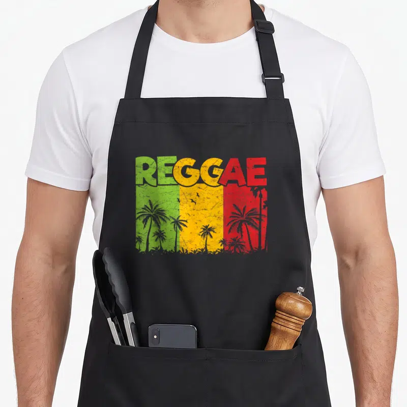 Tablier de cuisine noir avec inscription REGGAE aux couleurs du drapeau jamaïcain et silhouettes de palmiers.