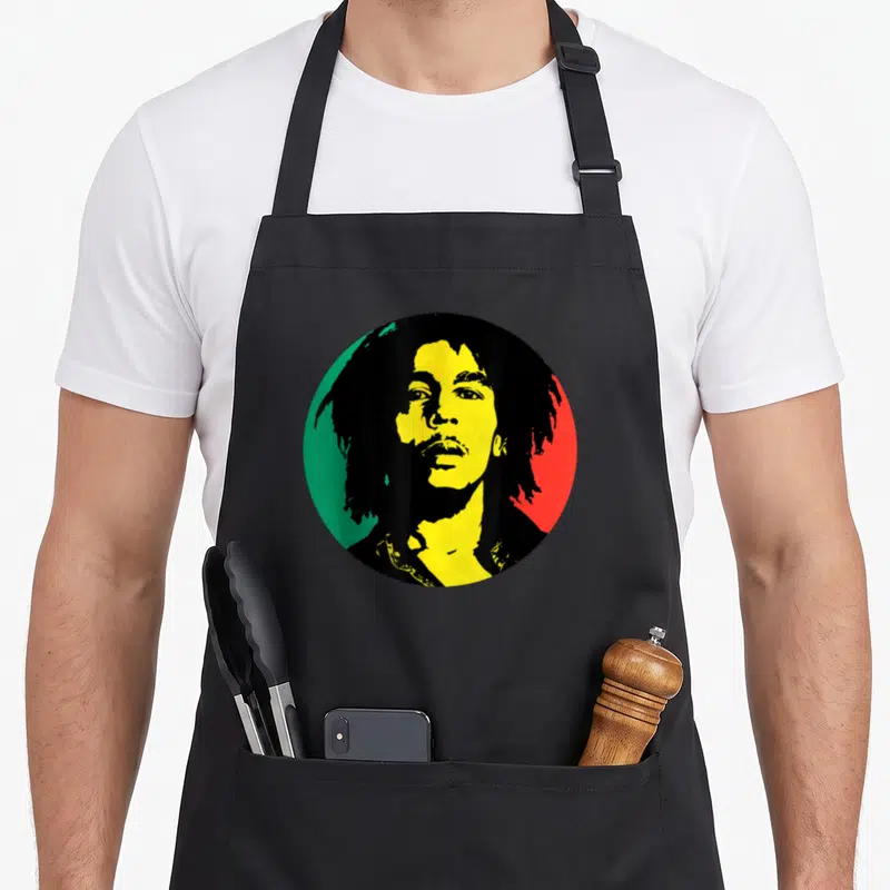 Tablier de cuisine noir avec un portrait circulaire de Bob Marley aux couleurs vert jaune et rouge rasta