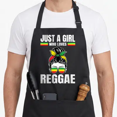 Tablier de cuisine noir avec illustration de fille aux lunettes aux couleurs Rasta et le texte Just a Girl who loves Reggae en blanc.