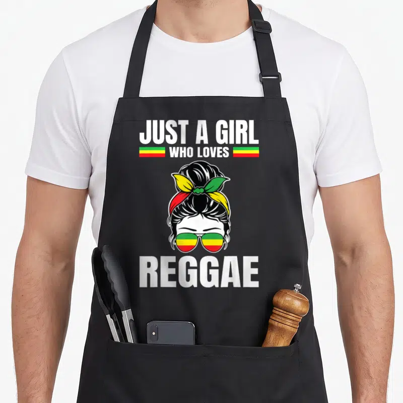 Tablier de cuisine noir avec illustration de fille aux lunettes aux couleurs Rasta et le texte Just a Girl who loves Reggae en blanc.