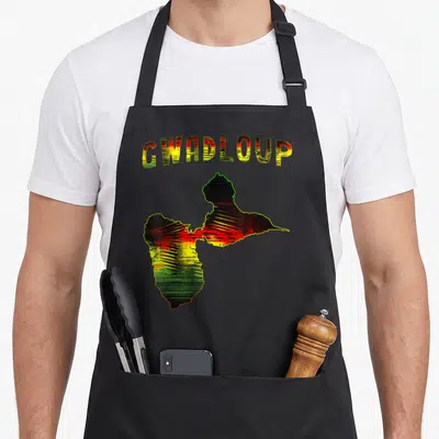 Tablier de cuisine noir avec carte de Gwadloup aux couleurs Rasta et texte stylisé en haut.