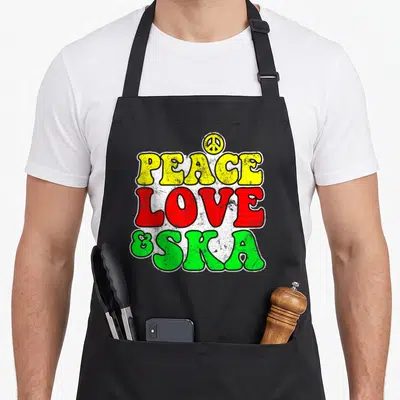 Tablier de cuisine noir avec l'inscription Peace Love & Ska aux couleurs vives et un logo de paix au sommet.