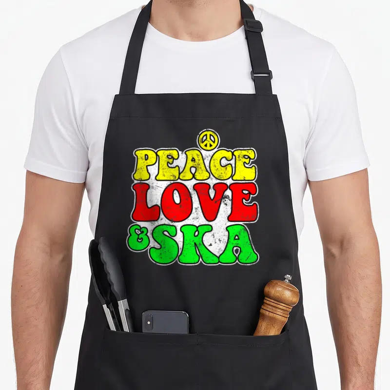 Tablier de cuisine noir avec l'inscription Peace Love & Ska aux couleurs vives et un logo de paix au sommet.