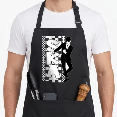Tablier de cuisine noir avec illustration d'un homme en costume et chapeau devant le mot Ska en lettres blanches sur fond damier.