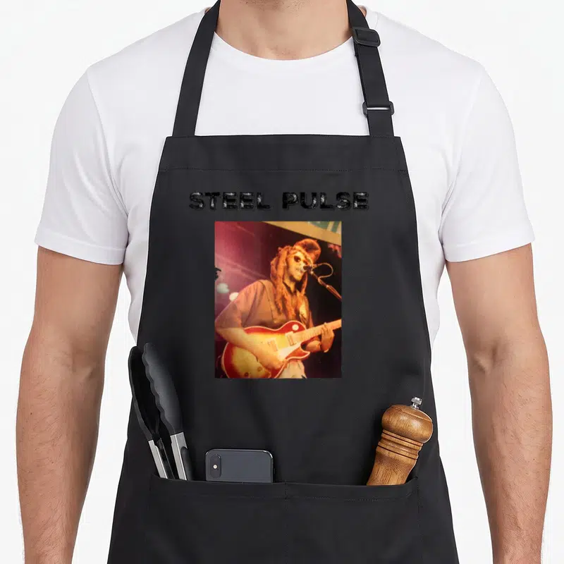 Tablier de cuisine noir avec une photo de David Hinds de Steel Pulse jouant de la guitare sous les projecteurs.