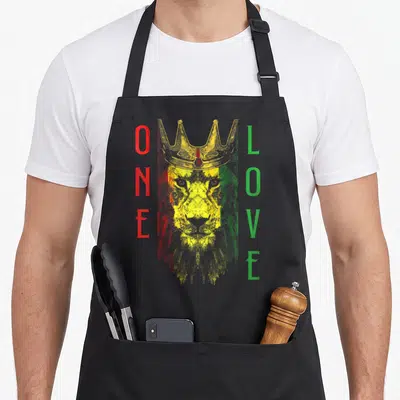 Tablier de cuisine noir avec un lion couronné aux couleurs Rasta et le texte One Love vertical.