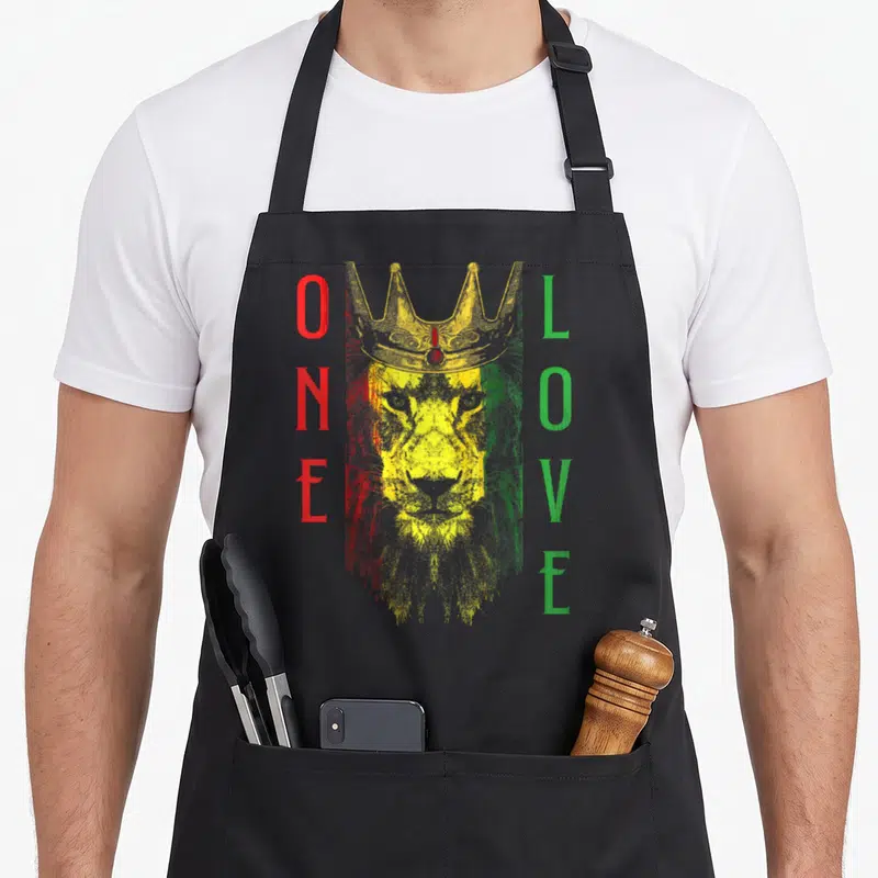 Tablier de cuisine noir avec un lion couronné aux couleurs Rasta et le texte One Love vertical.