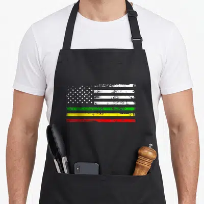 Tablier de cuisine noir avec un motif de drapeau aux étoiles blanches et bandes colorées vert jaune et rouge.
