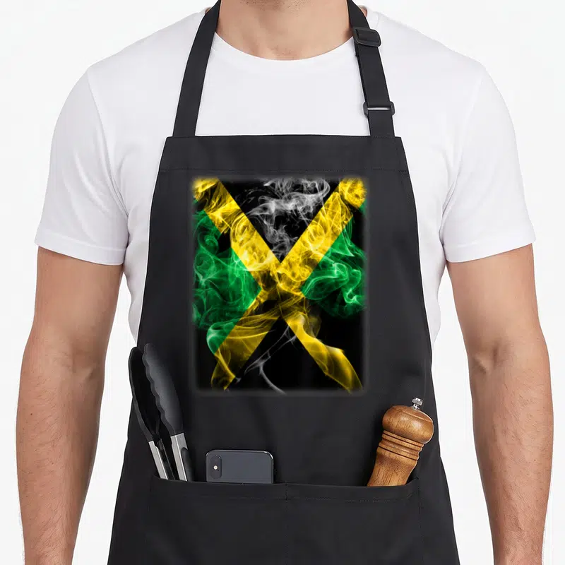 Tablier de cuisine noir avec un drapeau jamaïcain formé par des nuages de fumée colorés vert jaune et noir sur fond sombre.
