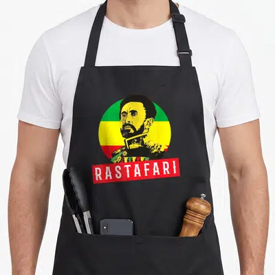 Tablier de cuisine noir avec illustration circulaire Rastafari et texte blanc sur bande rouge