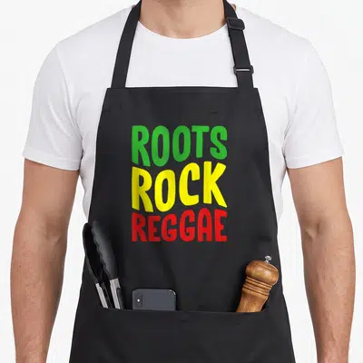 Tablier de cuisine noir avec linscription Roots Rock Reggae en lettres vertes jaunes et rouges superposées verticalement.