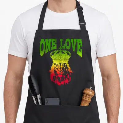 Tablier de cuisine noir avec tête de lion couronnée aux couleurs vert jaune rouge et texte One Love au-dessus.
