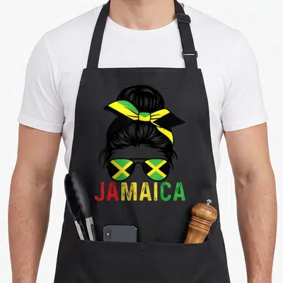 Tablier de cuisine noir avec une femme aux lunettes solaires au drapeau jamaïcain et un nœud dans les cheveux.