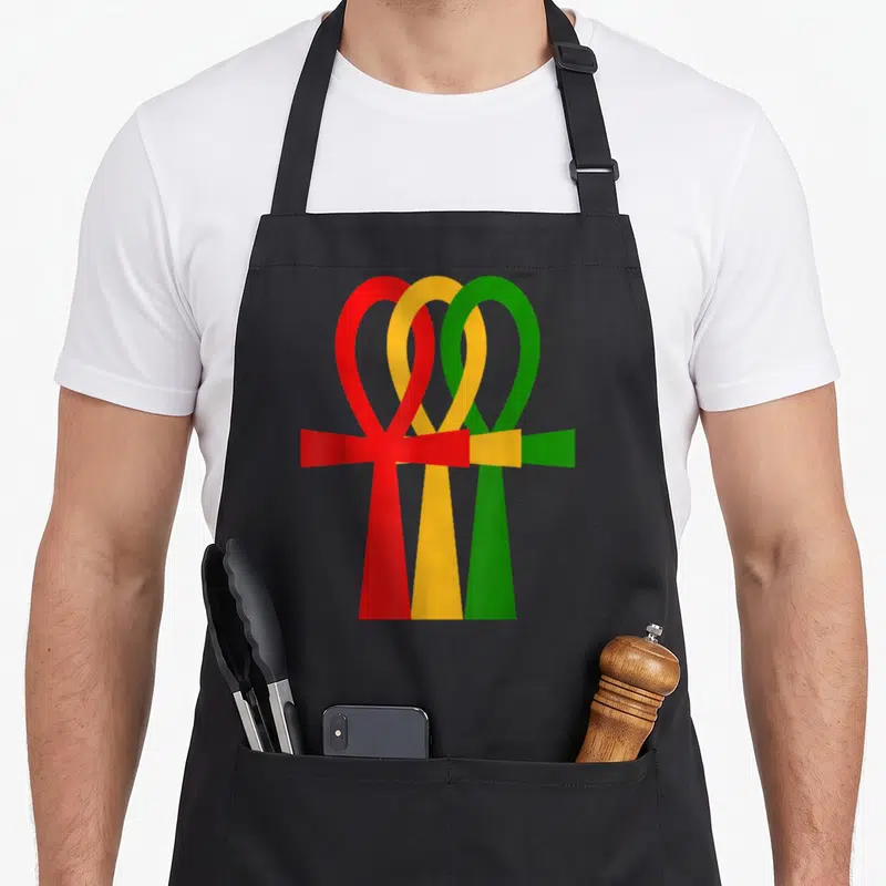 Tablier de cuisine noir avec trois symboles Ankh superposés rouges jaunes et verts sur fond uni.