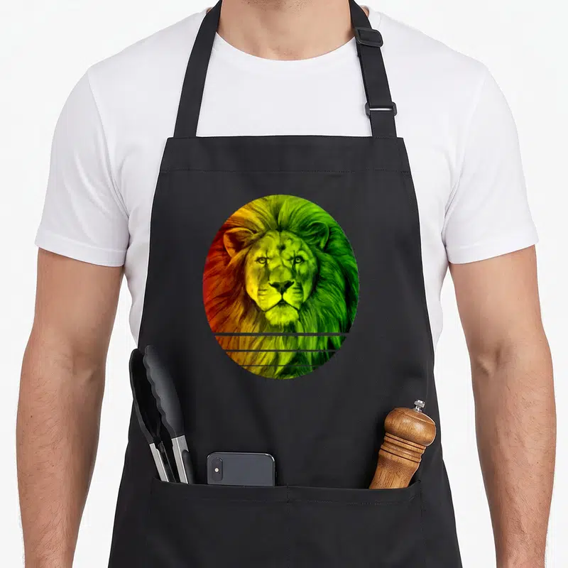 Tablier de cuisine noir avec un lion aux couleurs Rasta encadré dans un ovale aux teintes vert jaune et rouge.