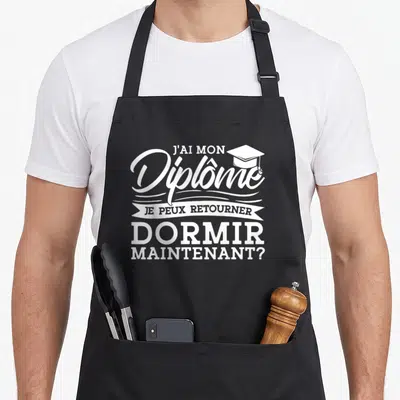 Tablier de cuisine noir avec inscription blanche J'ai mon diplôme Je peux aller dormir maintenant et une casquette d'étudiant.