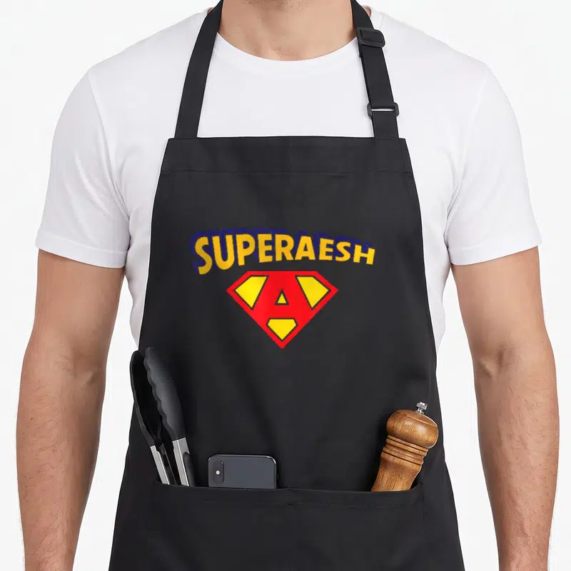 Tablier de cuisine noir avec le texte Super Aesh et un logo rouge jaune en forme de diamant sur la poitrine.
