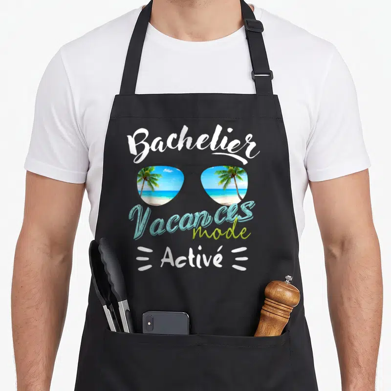 Tablier de cuisine noir avec lunettes de soleil reflétant des palmiers et le texte Vacances mode activé.