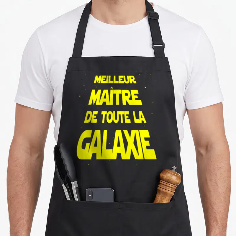 Tablier de cuisine noir avec l'inscription jaune Meilleur Maître de toute la Galaxie sur fond uni.