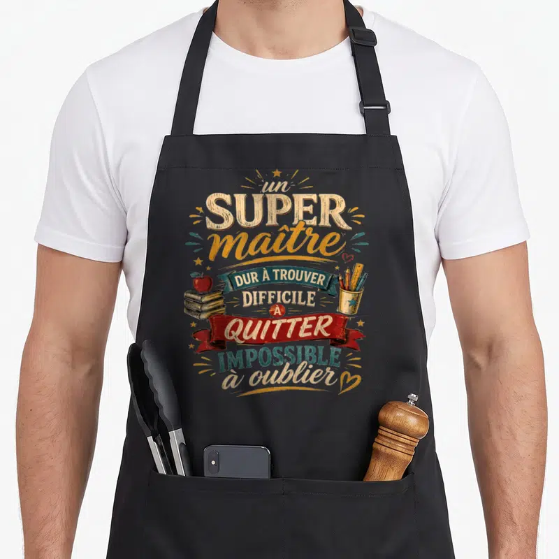Tablier de cuisine noir avec inscription Un Super Maître d'École, livres, pomme rouge et porte-crayons colorés sur fond gris uni.