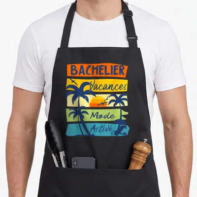 Tablier de cuisine noir avec illustration de palmiers et texte Bachelier Vacances Mode Activé sur bandes colorées.