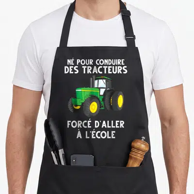 Tablier de cuisine noir avec illustration d'un tracteur vert et texte blanc sur fond uni.