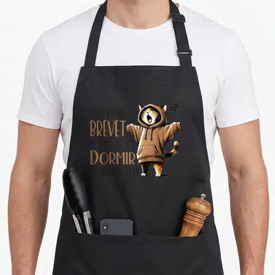 Tablier de cuisine noir avec un chat tricolore en pull à capuche et texte humoristique sur la réussite scolaire.