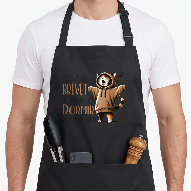 Tablier de cuisine noir avec un chat tricolore en pull à capuche et texte humoristique sur la réussite scolaire.