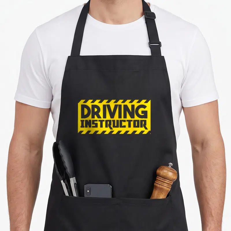 Tablier de cuisine noir avec logo jaune et gris portant linscription Driving Instructor encadré de bandes diagonales.