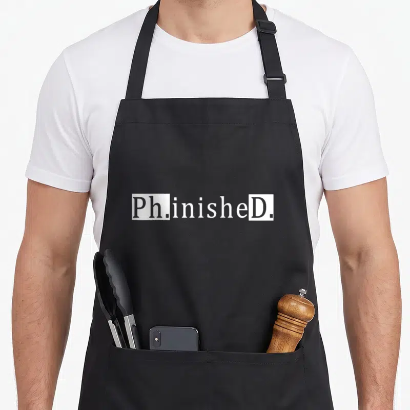 Tablier de cuisine noir avec l'inscription blanche Ph.inisheD. en typographie stylisée et blocs rectangulaires.