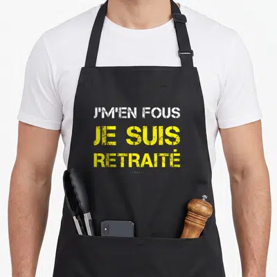 Tablier de cuisine noir avec inscription J'MEN FOUS JE SUIS RETRAITÉ en typographie blanche et jaune délavée.