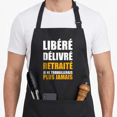Tablier de cuisine noir avec inscription blanche et orange proclamant Libéré Délivré Retraité et Je ne travaillerais plus jamais.