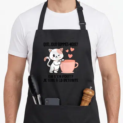 Tablier de cuisine noir avec un chat blanc et rose tenant une tasse rose et le texte On s'en fout je suis à la retraite.