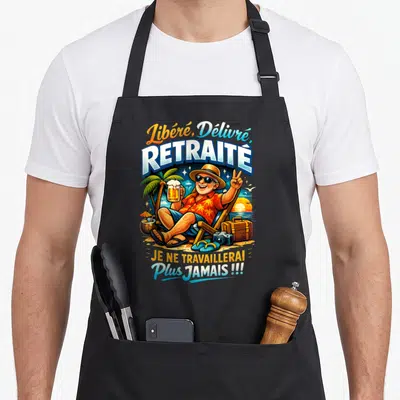 Tablier de cuisine noir illustrant un retraité souriant en chaise longue tenant une bière sous un palmier avec les mots Libéré et Délivré.