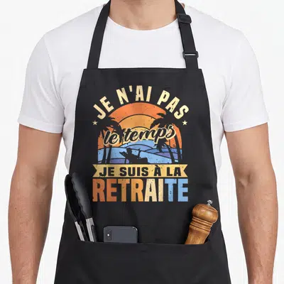 Tablier de cuisine noir avec une illustration retro d'un coucher de soleil et des palmiers au-dessus du texte imprimé.