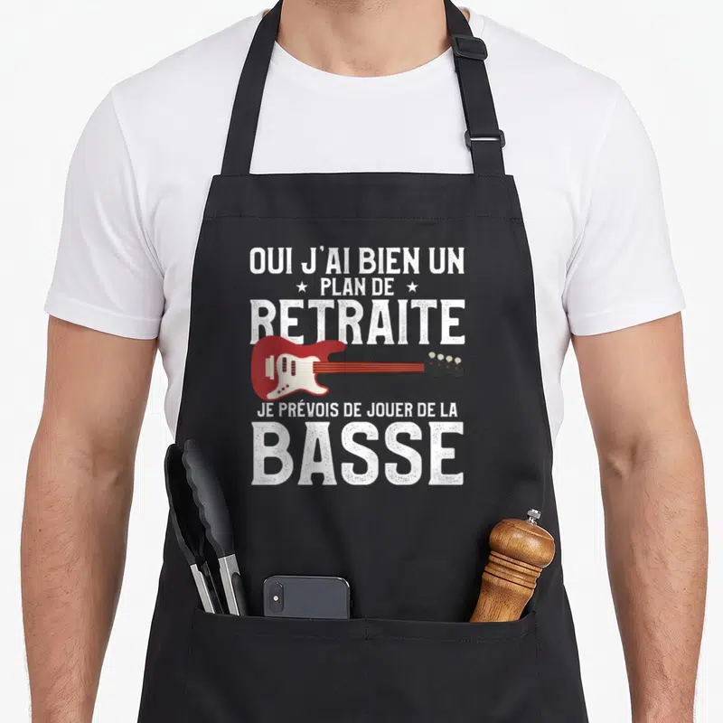 Tablier de cuisine noir avec texte blanc et illustration d'une guitare basse rouge sur fond uni.