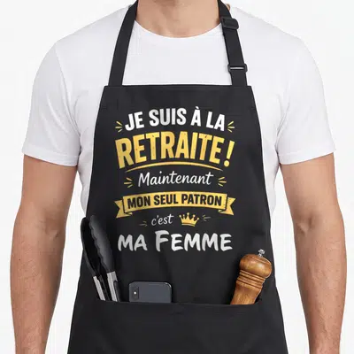 Tablier de cuisine noir avec l'inscription Je suis à la retraite mon seul patron c'est ma femme en jaune et blanc.